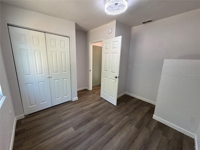 unfurnished bedroom with a closet, baseboards, dark wood finished floors, and visible vents