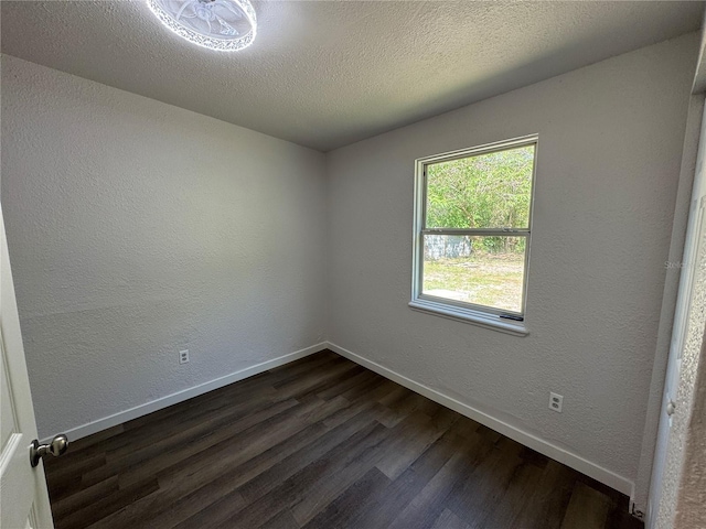spare room with a textured ceiling, dark wood-style flooring, baseboards, and a textured wall