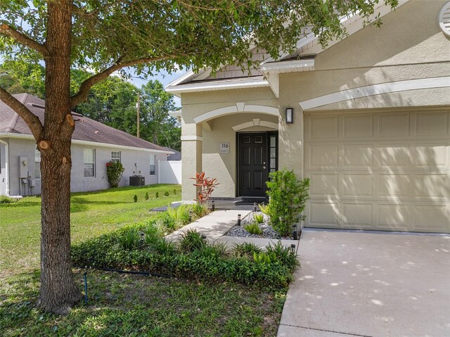 view of exterior entry featuring central air condition unit, a garage, a lawn, stucco siding, and driveway