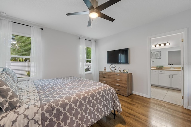 bedroom featuring ensuite bathroom, ceiling fan, multiple windows, and light wood-style floors