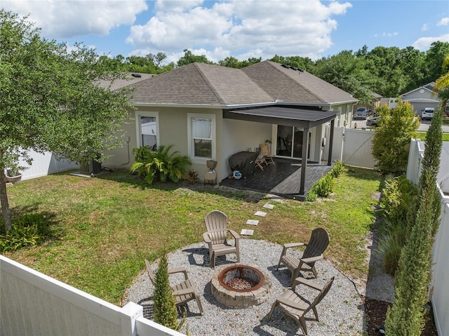 rear view of house with a yard, a fenced backyard, stucco siding, roof with shingles, and a fire pit