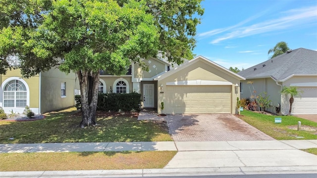 view of front of property featuring stucco siding, an attached garage, a front lawn, and decorative driveway