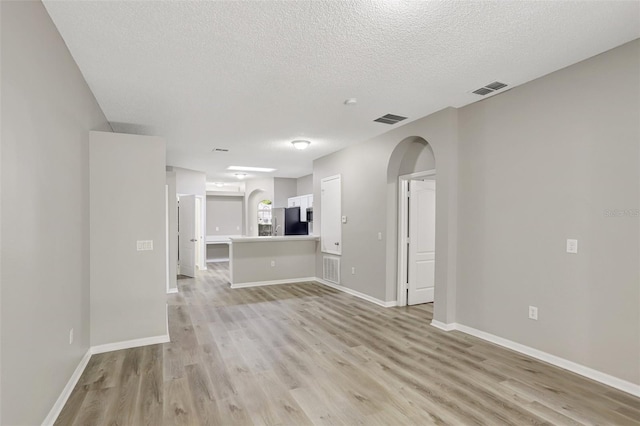 unfurnished living room with light wood-style flooring, baseboards, visible vents, and arched walkways