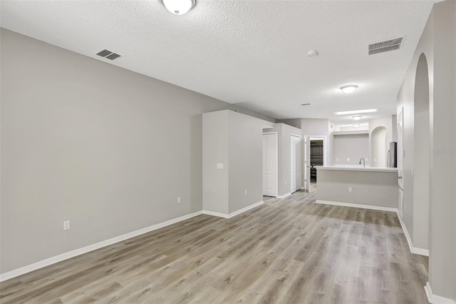 unfurnished living room with arched walkways, baseboards, visible vents, and light wood finished floors