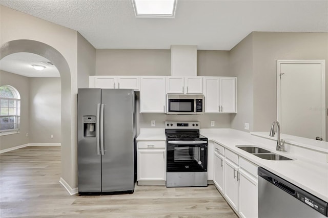 kitchen with appliances with stainless steel finishes, arched walkways, white cabinetry, a sink, and light wood-type flooring