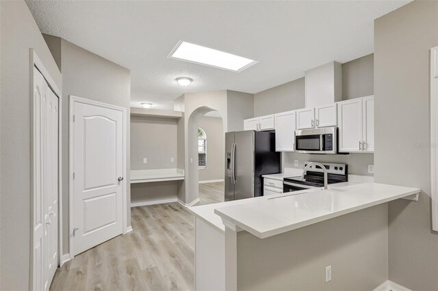 kitchen featuring white cabinetry, light countertops, stainless steel appliances, arched walkways, and light wood-style floors