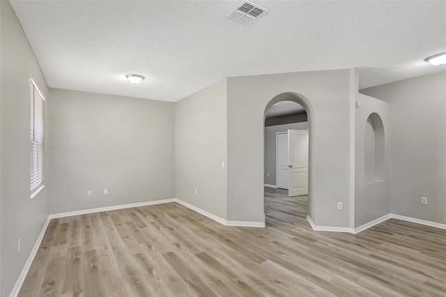 unfurnished room with light wood finished floors, visible vents, arched walkways, and a textured ceiling