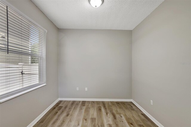 unfurnished room featuring light wood finished floors, baseboards, and a textured ceiling