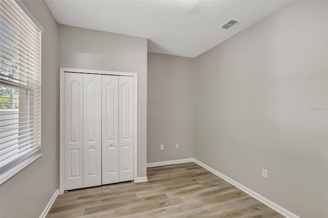 unfurnished bedroom with a closet, a textured ceiling, light wood-type flooring, baseboards, and visible vents