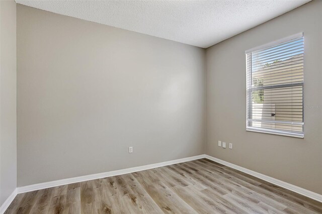 spare room with baseboards, light wood finished floors, and a textured ceiling