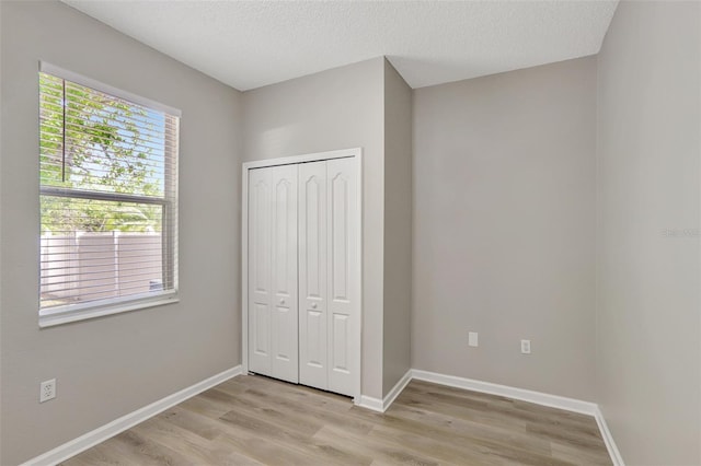unfurnished bedroom with baseboards, a textured ceiling, a closet, and light wood-type flooring