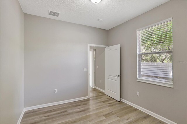 empty room featuring baseboards, visible vents, light wood-style flooring, and a textured ceiling