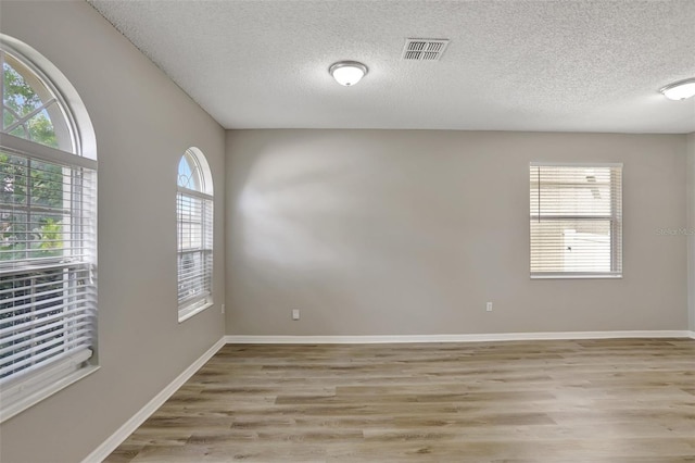 empty room with baseboards, a textured ceiling, visible vents, and light wood finished floors