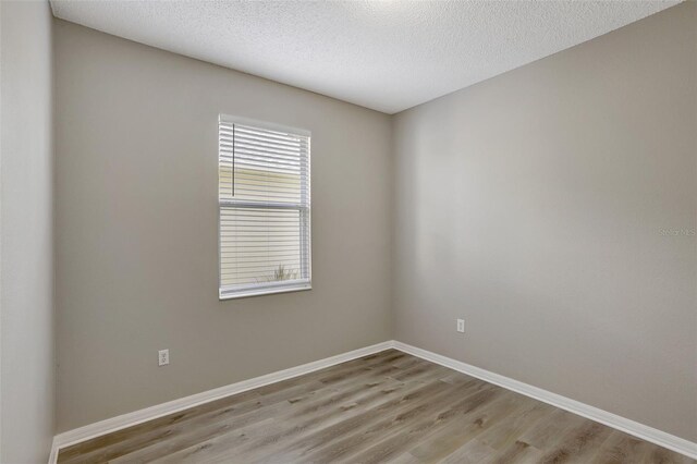 empty room with a textured ceiling, baseboards, and light wood-type flooring