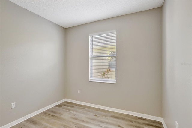 spare room with light wood-style flooring, baseboards, and a textured ceiling