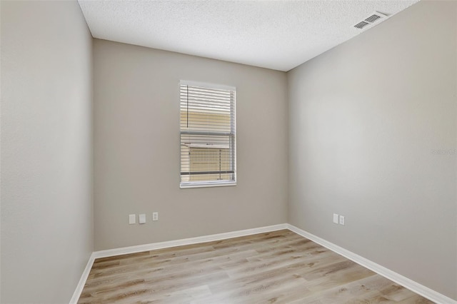 unfurnished room featuring baseboards, a textured ceiling, visible vents, and light wood-style floors