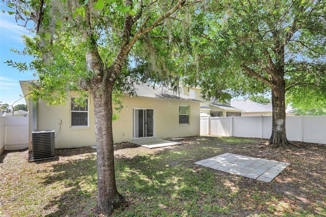 rear view of house with a fenced backyard, stucco siding, and central AC