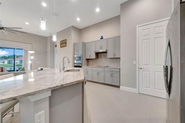 kitchen featuring tasteful backsplash, appliances with stainless steel finishes, under cabinet range hood, a sink, and gray cabinetry