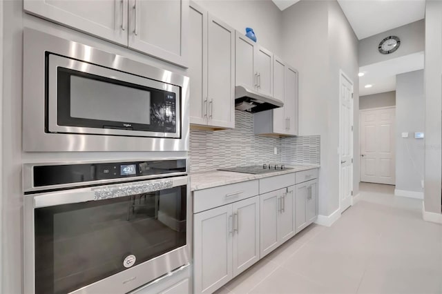 kitchen with baseboards, appliances with stainless steel finishes, under cabinet range hood, backsplash, and light tile patterned floors