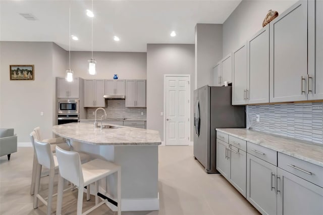 kitchen featuring gray cabinetry, a kitchen bar, a sink, and stainless steel appliances