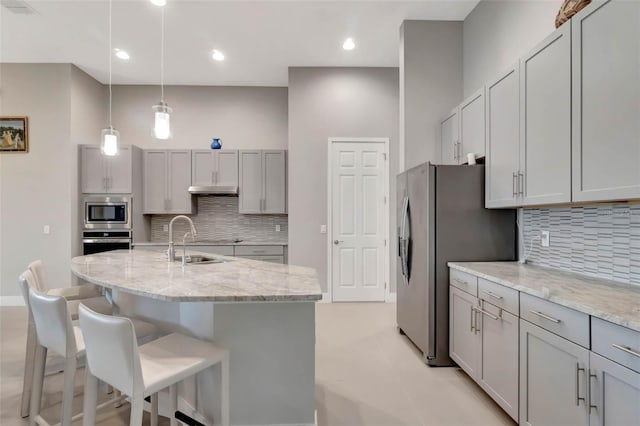 kitchen with a breakfast bar area, stainless steel appliances, hanging light fixtures, a sink, and light stone countertops