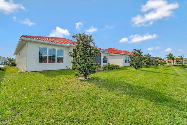 back of property with stucco siding, a tile roof, and a lawn