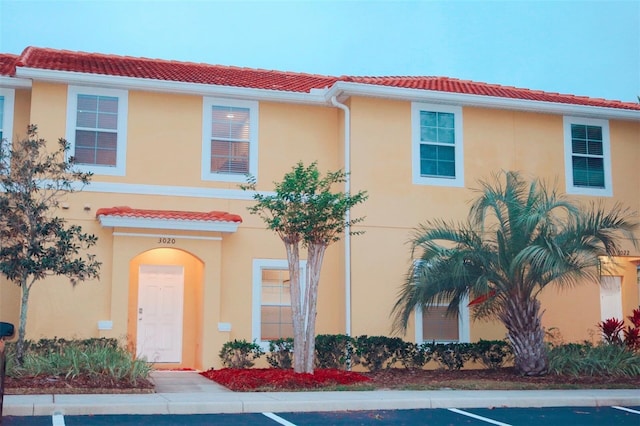 view of front of house featuring stucco siding, a tile roof, and uncovered parking