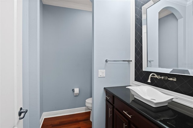 bathroom featuring wood finished floors, toilet, vanity, baseboards, and decorative backsplash