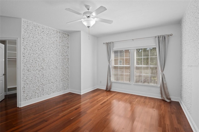 unfurnished room with wallpapered walls, wood finished floors, a ceiling fan, and baseboards