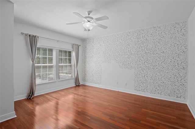 unfurnished room with wallpapered walls, a ceiling fan, wood finished floors, and baseboards