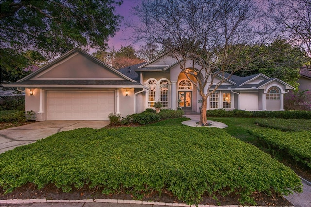 view of front of house featuring a garage, stucco siding, a front lawn, french doors, and driveway
