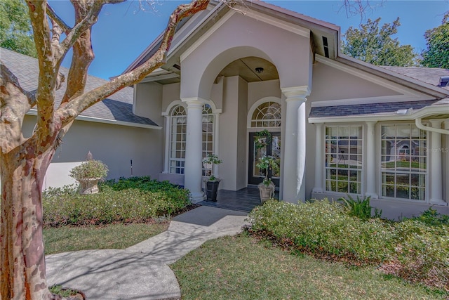 view of exterior entry featuring a shingled roof and stucco siding