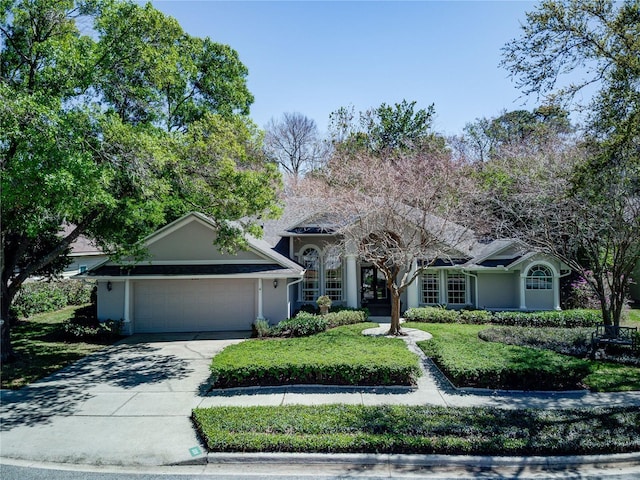 view of front of house with concrete driveway, an attached garage, a front lawn, and stucco siding