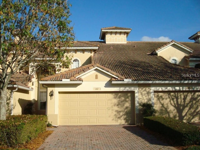 mediterranean / spanish-style house with driveway, a tiled roof, stucco siding, and an attached garage