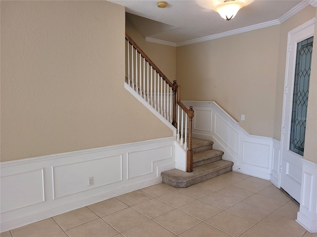 stairs with a decorative wall, wainscoting, ornamental molding, and tile patterned floors