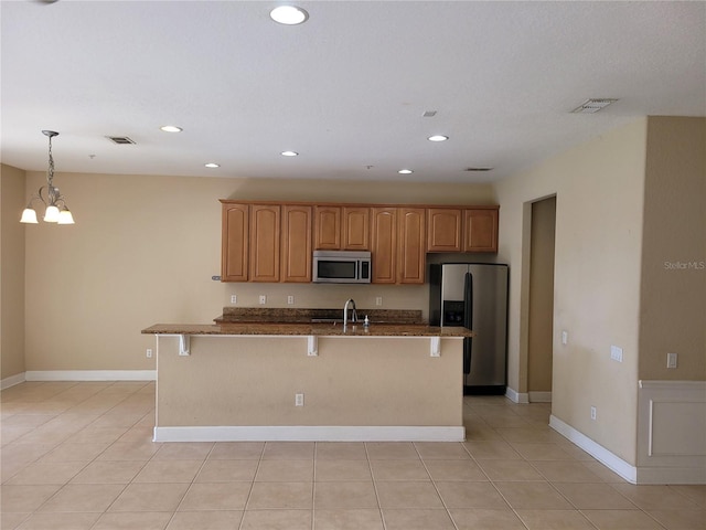 kitchen with appliances with stainless steel finishes, a sink, a kitchen bar, recessed lighting, and dark stone countertops