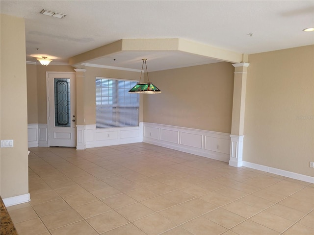 spare room with decorative columns, a decorative wall, ornamental molding, a wainscoted wall, and light tile patterned floors
