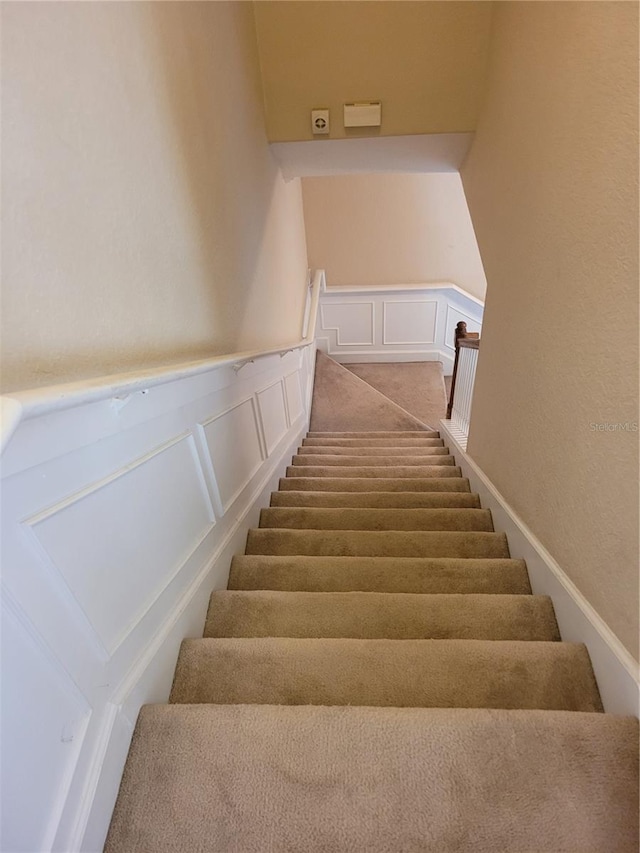 stairway featuring a decorative wall and a wainscoted wall