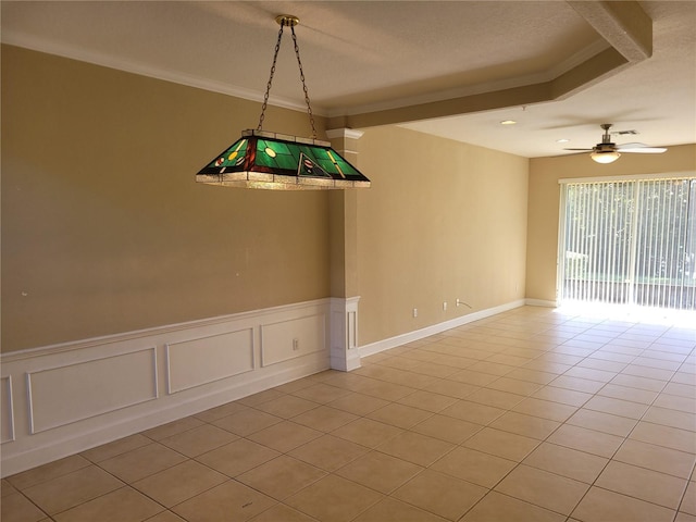 empty room featuring ceiling fan, crown molding, light tile patterned flooring, wainscoting, and a decorative wall