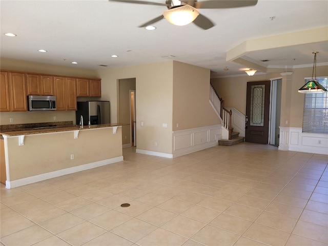 kitchen featuring stainless steel appliances, open floor plan, a ceiling fan, a kitchen bar, and light tile patterned flooring