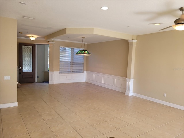 spare room featuring ornate columns, a decorative wall, light tile patterned flooring, a ceiling fan, and a wainscoted wall