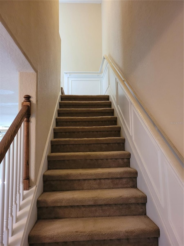 stairs with a decorative wall, a textured wall, and wainscoting