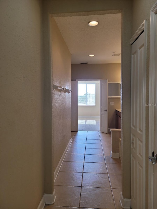 hall featuring baseboards, light tile patterned floors, and recessed lighting
