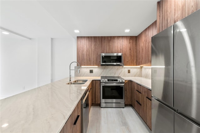 kitchen featuring light stone counters, a sink, appliances with stainless steel finishes, modern cabinets, and brown cabinetry