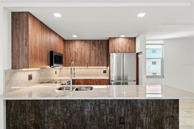 kitchen featuring a sink, light stone counters, brown cabinetry, and appliances with stainless steel finishes