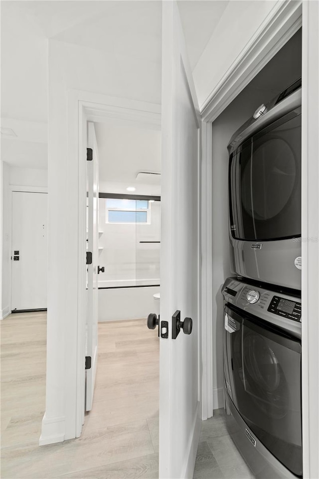 laundry area featuring light wood finished floors, stacked washer and clothes dryer, and laundry area