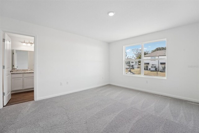 unfurnished bedroom with baseboards, ensuite bath, and carpet