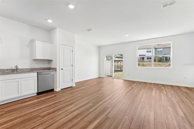 unfurnished living room with baseboards, light wood-type flooring, visible vents, and a sink