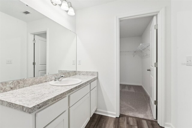bathroom featuring vanity, wood finished floors, a walk in closet, baseboards, and visible vents