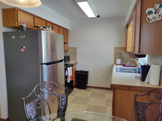 kitchen with appliances with stainless steel finishes, tasteful backsplash, brown cabinets, a sink, and light countertops
